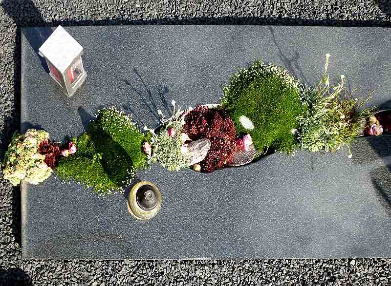 Schön bepflanzte Steinplatte auf Grab